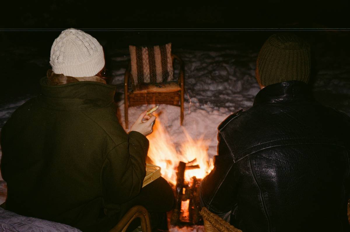 Two people sit by a campfire at night.