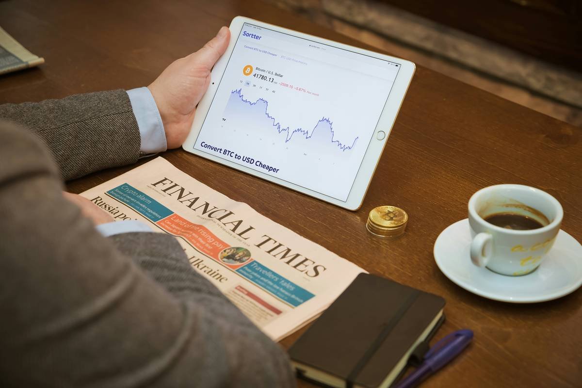 Drinking coffee in a coffee shop checking Bitcoin chart with Financial Times, from United Kingdom, aside.